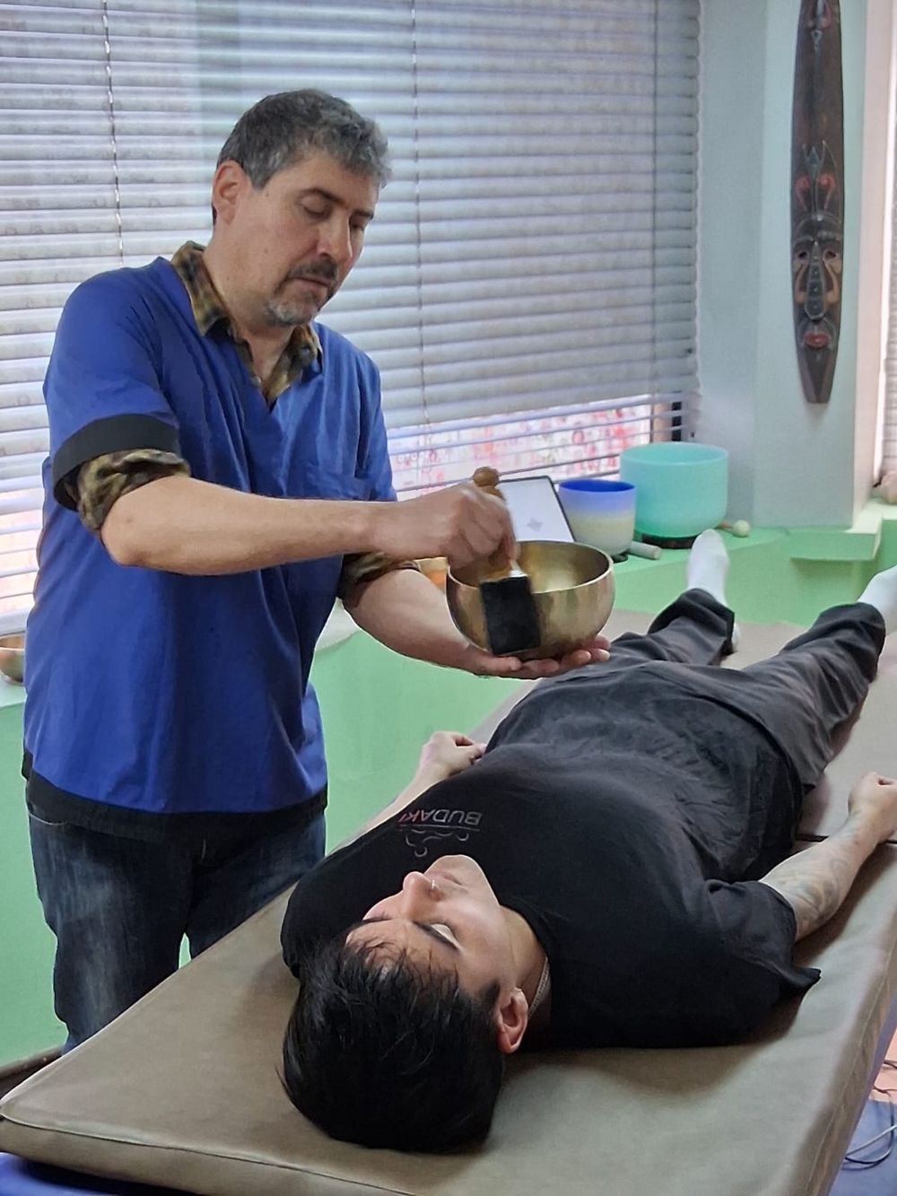 Reinaldo Farías con un cuenco tibetano junto a una persona recostada sobre el Mat Vibroacústico